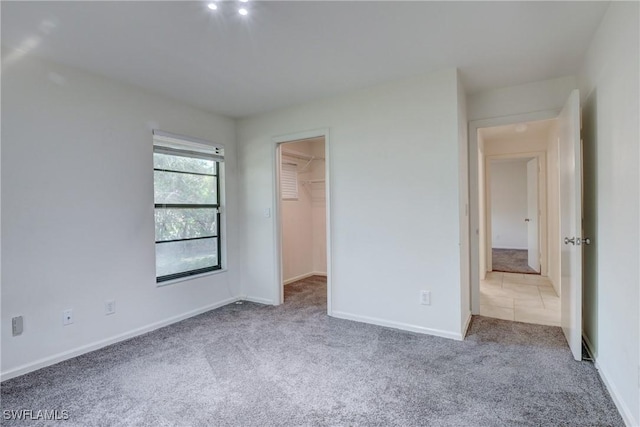 unfurnished bedroom featuring a walk in closet, light colored carpet, and a closet