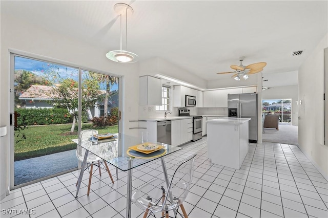 kitchen featuring light tile patterned floors, stainless steel appliances, a center island, white cabinets, and decorative light fixtures