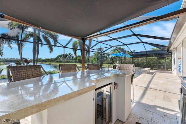 view of patio / terrace featuring a water view, area for grilling, glass enclosure, a bar, and beverage cooler