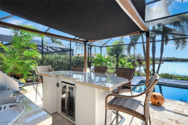 view of patio with beverage cooler, an outdoor bar, glass enclosure, and a water view