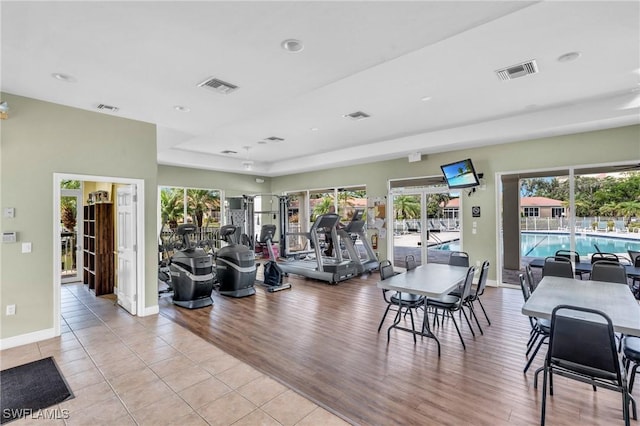 workout area featuring a tray ceiling and light hardwood / wood-style flooring