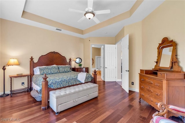 bedroom featuring dark hardwood / wood-style flooring, connected bathroom, a raised ceiling, and ceiling fan