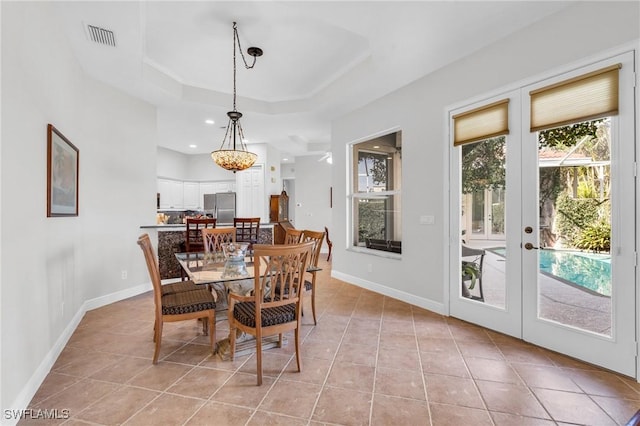 tiled dining space featuring a tray ceiling and french doors