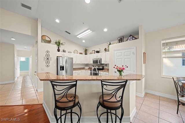 kitchen with stainless steel appliances, light stone counters, white cabinets, a kitchen bar, and a large island with sink