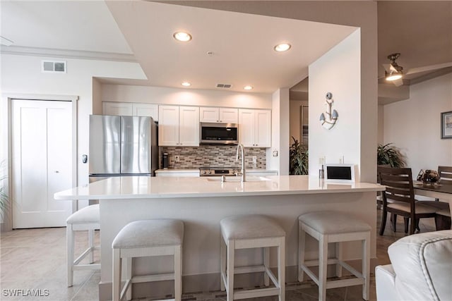 kitchen featuring sink, a breakfast bar area, appliances with stainless steel finishes, white cabinets, and backsplash