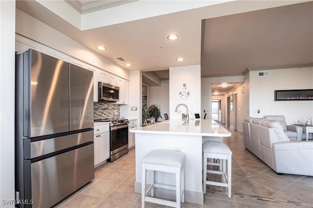 kitchen with a kitchen bar, a center island with sink, stainless steel appliances, decorative backsplash, and white cabinets