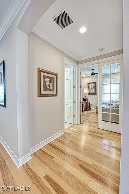 corridor with arched walkways, visible vents, baseboards, ornamental molding, and light wood finished floors