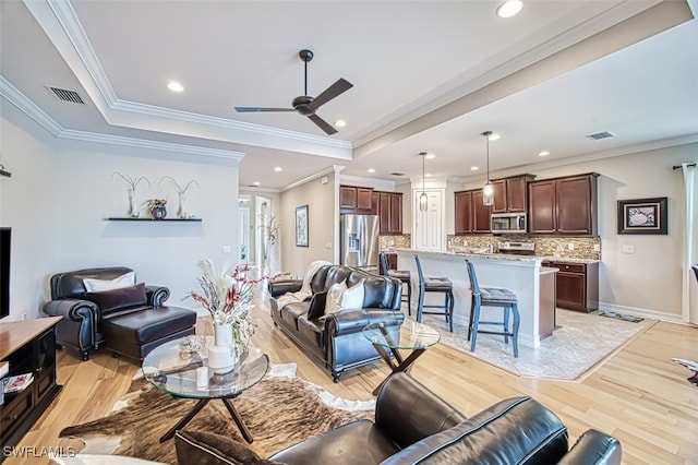 living area featuring light wood-type flooring, a tray ceiling, and visible vents