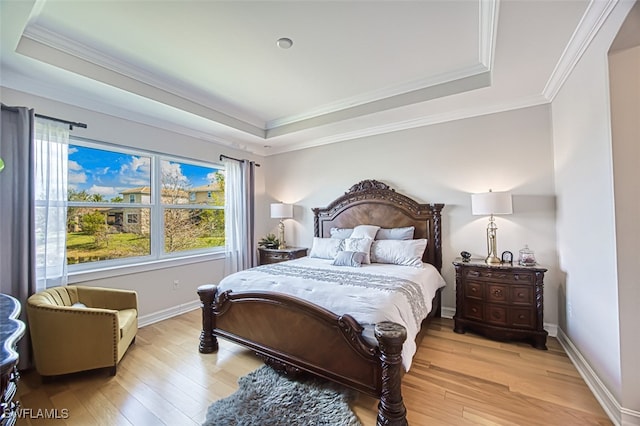 bedroom with light wood finished floors, baseboards, and a tray ceiling