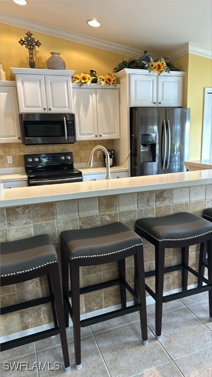 kitchen with stainless steel appliances, a breakfast bar, ornamental molding, and decorative backsplash