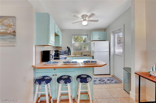 kitchen with light tile patterned floors, a peninsula, a breakfast bar, freestanding refrigerator, and stainless steel microwave