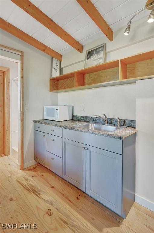 kitchen with white microwave, beamed ceiling, gray cabinetry, light wood-style floors, and open shelves