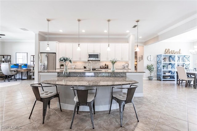 kitchen featuring white cabinetry, appliances with stainless steel finishes, a kitchen island with sink, and hanging light fixtures