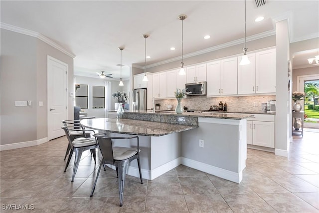 kitchen featuring a breakfast bar area, appliances with stainless steel finishes, a kitchen island with sink, dark stone countertops, and white cabinets