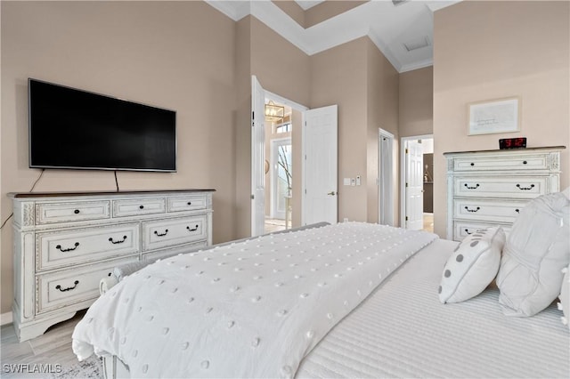 bedroom featuring crown molding, light wood finished floors, and ensuite bathroom