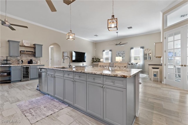 kitchen featuring beverage cooler, gray cabinets, a sink, open floor plan, and arched walkways