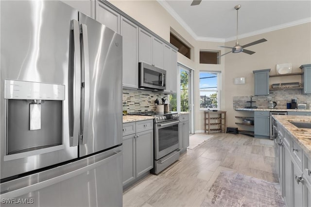 kitchen with gray cabinets, ceiling fan, stainless steel appliances, crown molding, and tasteful backsplash