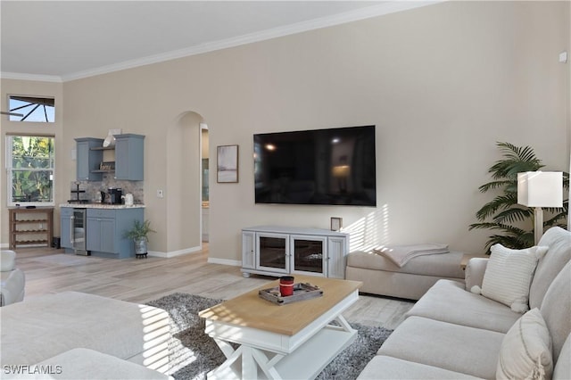 living room with arched walkways, light wood finished floors, crown molding, and baseboards