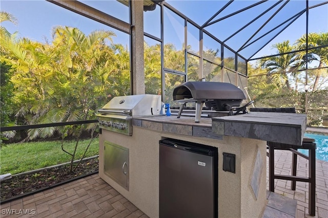 view of patio with a lanai, an outdoor pool, a grill, and exterior kitchen