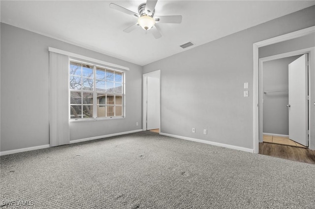 spare room featuring baseboards, visible vents, dark colored carpet, and a ceiling fan