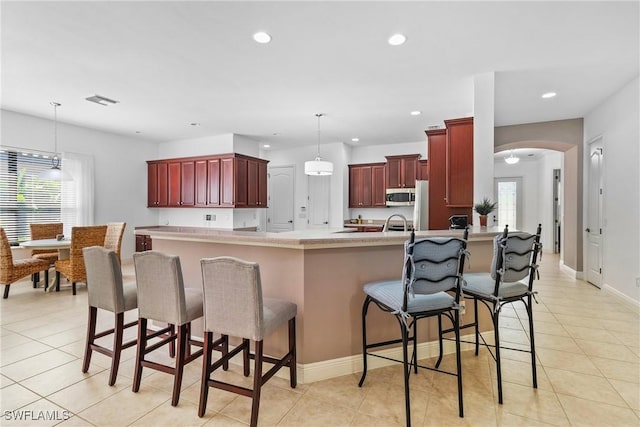 kitchen with arched walkways, stainless steel microwave, decorative light fixtures, light countertops, and dark brown cabinets