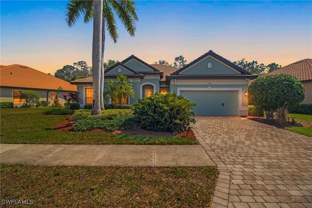 view of front of home with a garage, a lawn, decorative driveway, and stucco siding