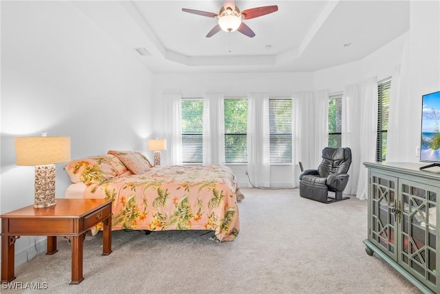 bedroom with multiple windows, visible vents, a tray ceiling, and light colored carpet