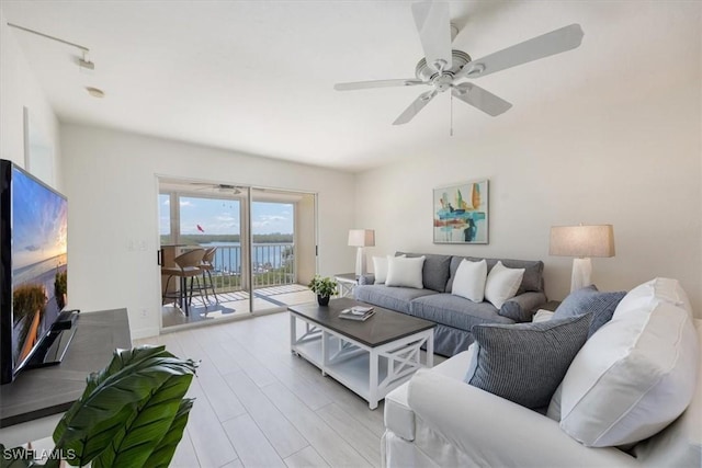 living room featuring light hardwood / wood-style floors, ceiling fan, and a water view