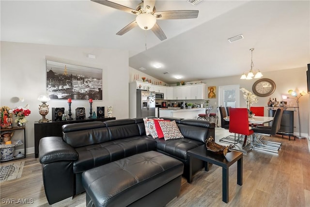 living room with ceiling fan with notable chandelier, vaulted ceiling, and light wood-type flooring