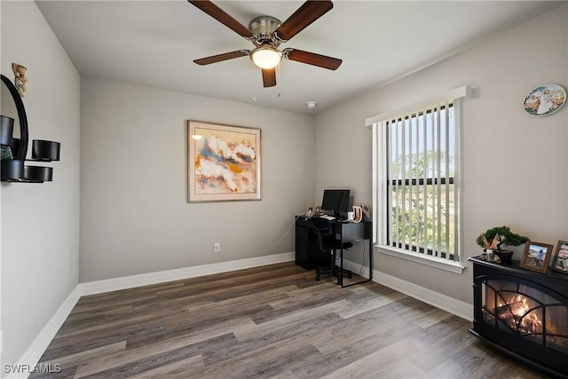 office area featuring wood-type flooring, ceiling fan, and a wood stove