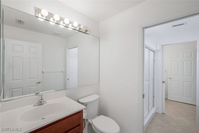 bathroom with a shower with door, vanity, tile patterned floors, and toilet