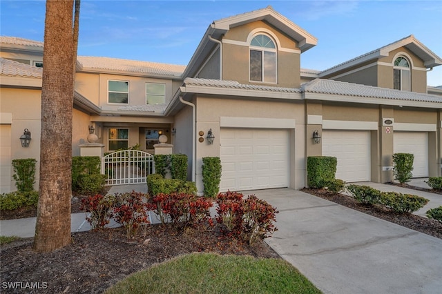 townhome / multi-family property with concrete driveway, a tiled roof, an attached garage, and stucco siding