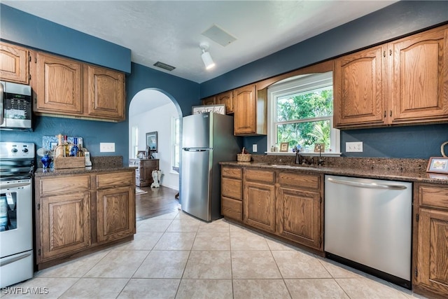 kitchen with stainless steel appliances, dark stone countertops, sink, and light tile patterned floors