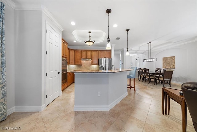 kitchen featuring crown molding, a center island with sink, stainless steel fridge, and decorative light fixtures