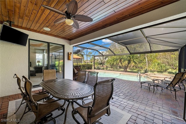 view of patio featuring ceiling fan, a swimming pool with hot tub, and glass enclosure