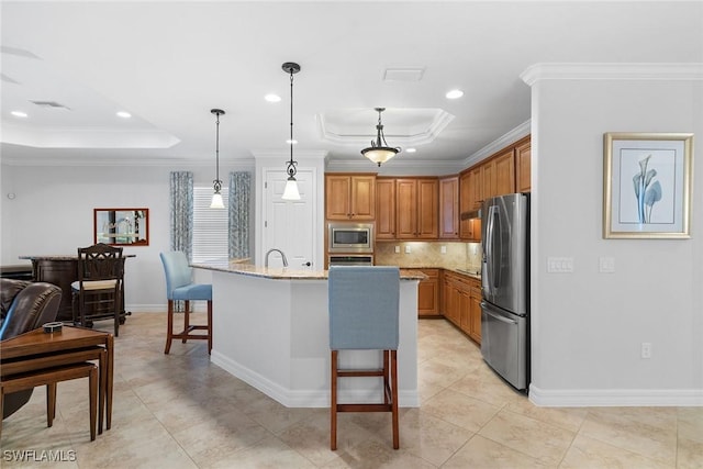 kitchen with pendant lighting, stainless steel appliances, light stone countertops, an island with sink, and a raised ceiling