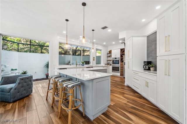 kitchen featuring a breakfast bar area, dark hardwood / wood-style flooring, pendant lighting, a large island, and white cabinets