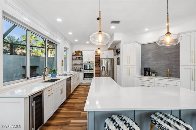 kitchen featuring white cabinetry, appliances with stainless steel finishes, decorative light fixtures, and beverage cooler