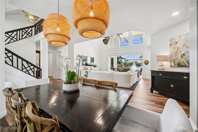 dining room with a towering ceiling, wood-type flooring, and decorative columns