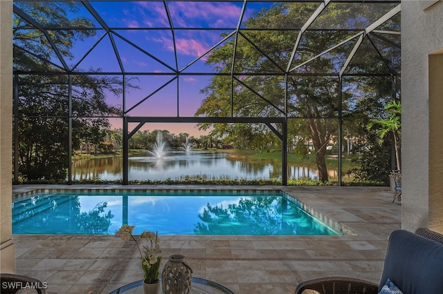 pool at dusk featuring a water view, a patio area, and a lanai