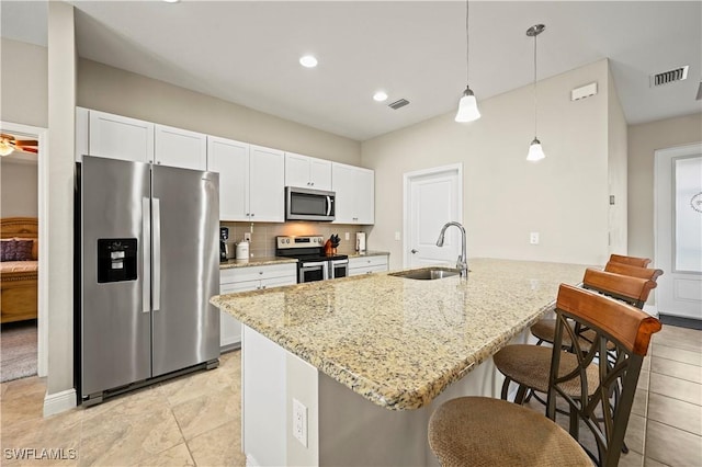 kitchen with pendant lighting, sink, white cabinetry, stainless steel appliances, and light stone counters