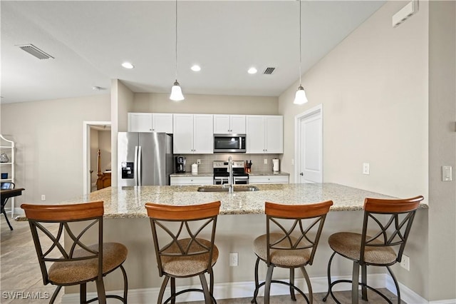 kitchen featuring appliances with stainless steel finishes, decorative light fixtures, tasteful backsplash, white cabinets, and a kitchen bar