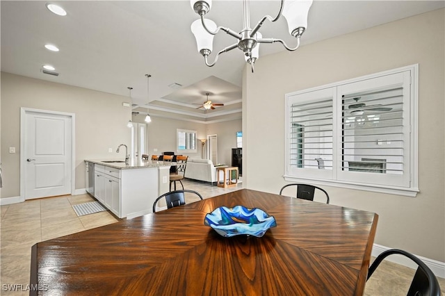 dining space with a raised ceiling, ceiling fan with notable chandelier, sink, and light tile patterned floors