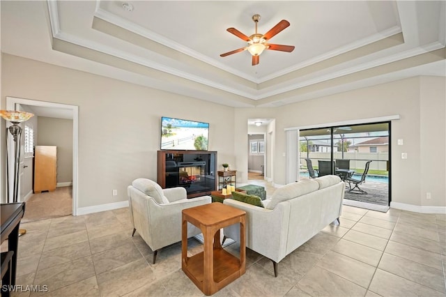 living room with a raised ceiling, ornamental molding, light tile patterned flooring, and ceiling fan