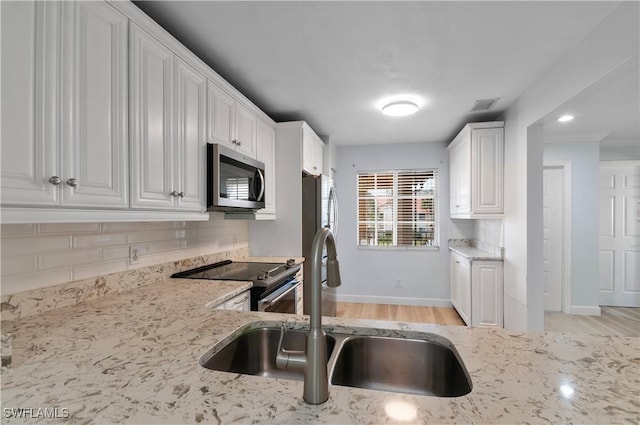 kitchen with sink, light hardwood / wood-style flooring, appliances with stainless steel finishes, white cabinets, and decorative backsplash