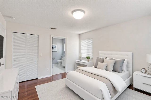 bedroom with dark wood-type flooring, a closet, a textured ceiling, and ensuite bathroom