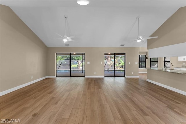 unfurnished living room featuring high vaulted ceiling, sink, ceiling fan, and light hardwood / wood-style flooring