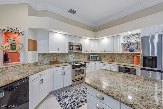 kitchen featuring crown molding, appliances with stainless steel finishes, white cabinetry, light stone counters, and beverage cooler