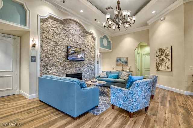 living room with crown molding, a stone fireplace, wood-type flooring, and a tray ceiling