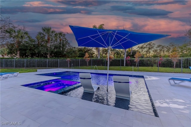 pool at dusk with a jacuzzi and a patio